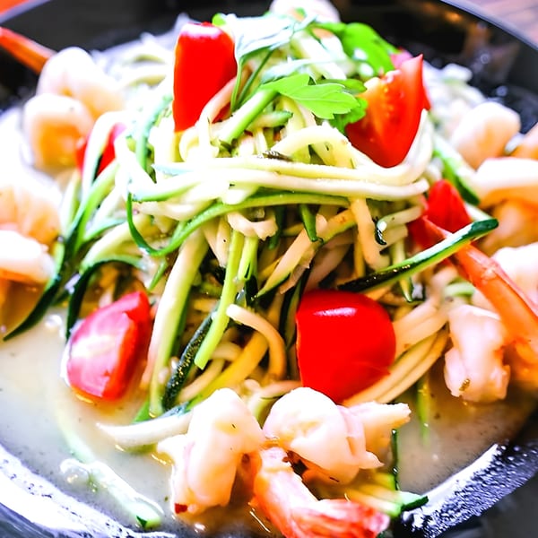 Shrimp ceviche with zucchini noodles, cherry tomatoes, and cilantro in a black bowl.
