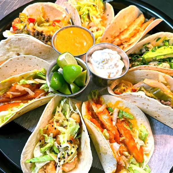 A platter of diverse Westchester Taco Grill tacos with various fillings, sauces, and lime wedges.