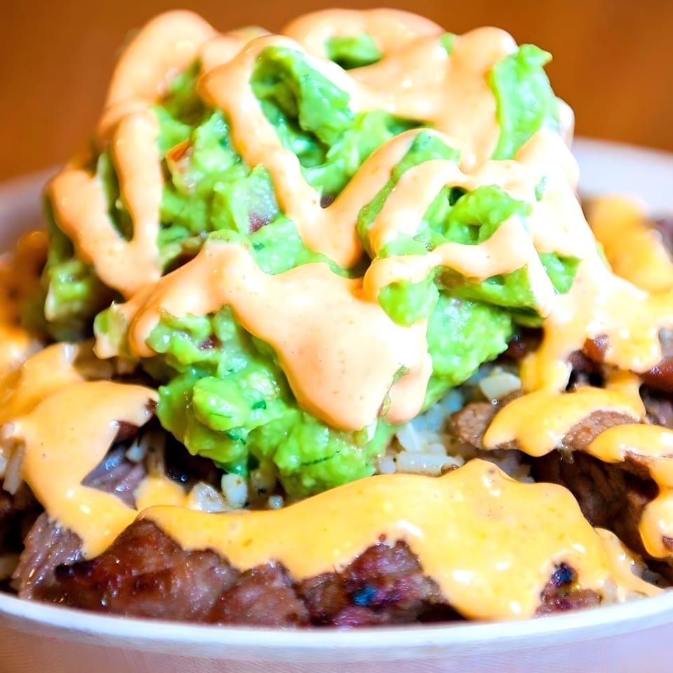 Close-up of a Westchester Taco Grill burrito bowl with steak, rice, guacamole, and orange sauce.